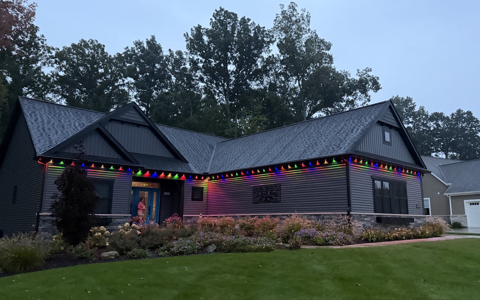 Charcoal craftsman home with its roofline lit in rainbow colors